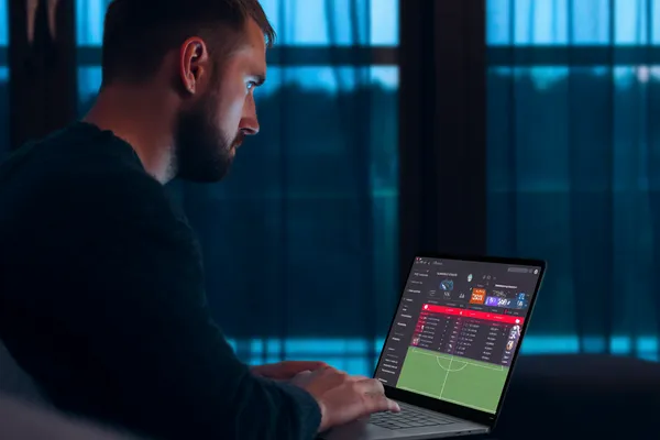 BDKK Mobile App — Your complete hub for casino and sports A man focused on his laptop with live stats in the background, highlighting the dedicated sports and gaming features of the BDKK mobile app.